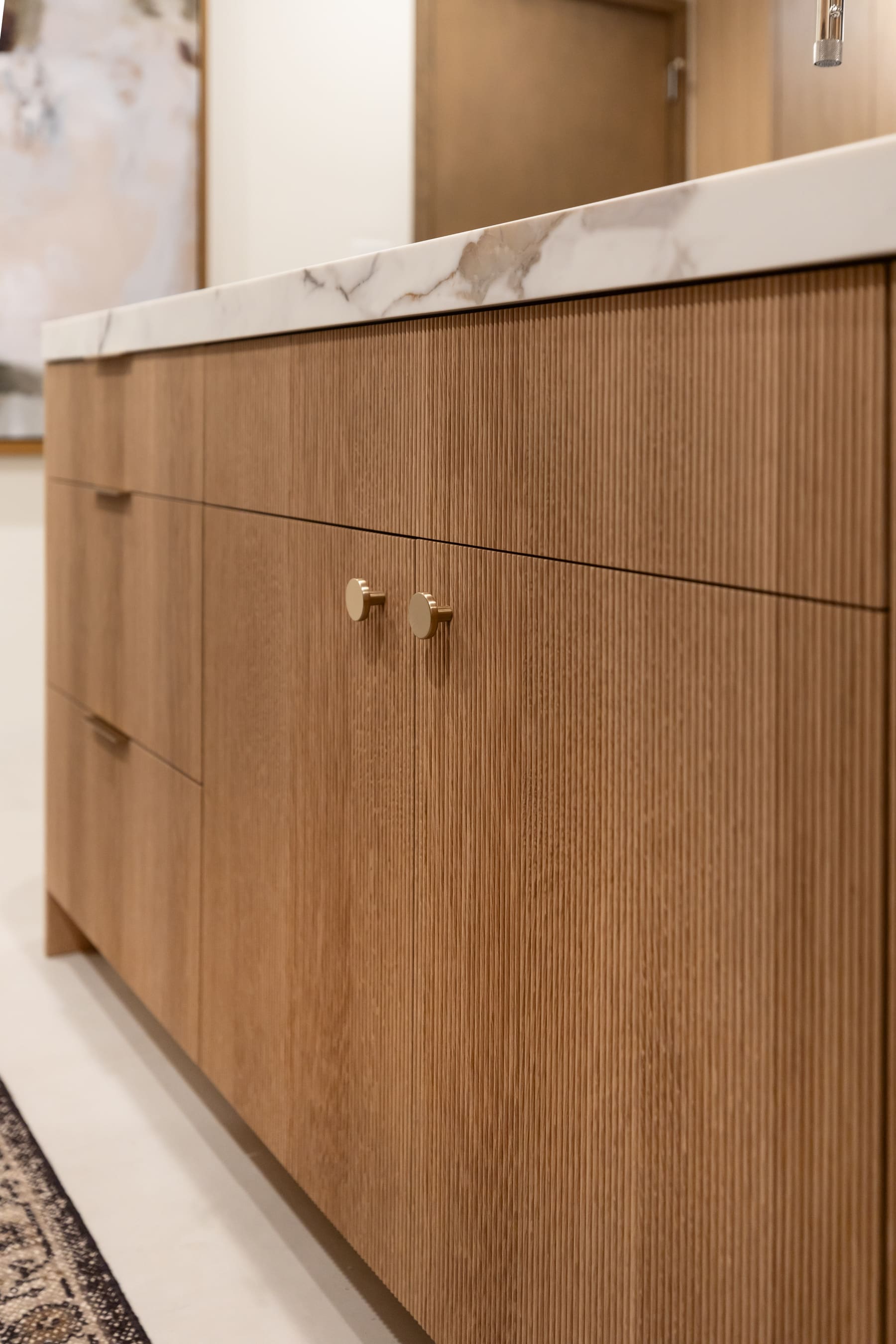 Reeded white oak island doors with brass knobs, marble top detail — Phoenix custom cabinetry